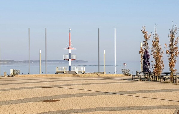 A coastal promenade with a lighthouse, benches, and a statue.