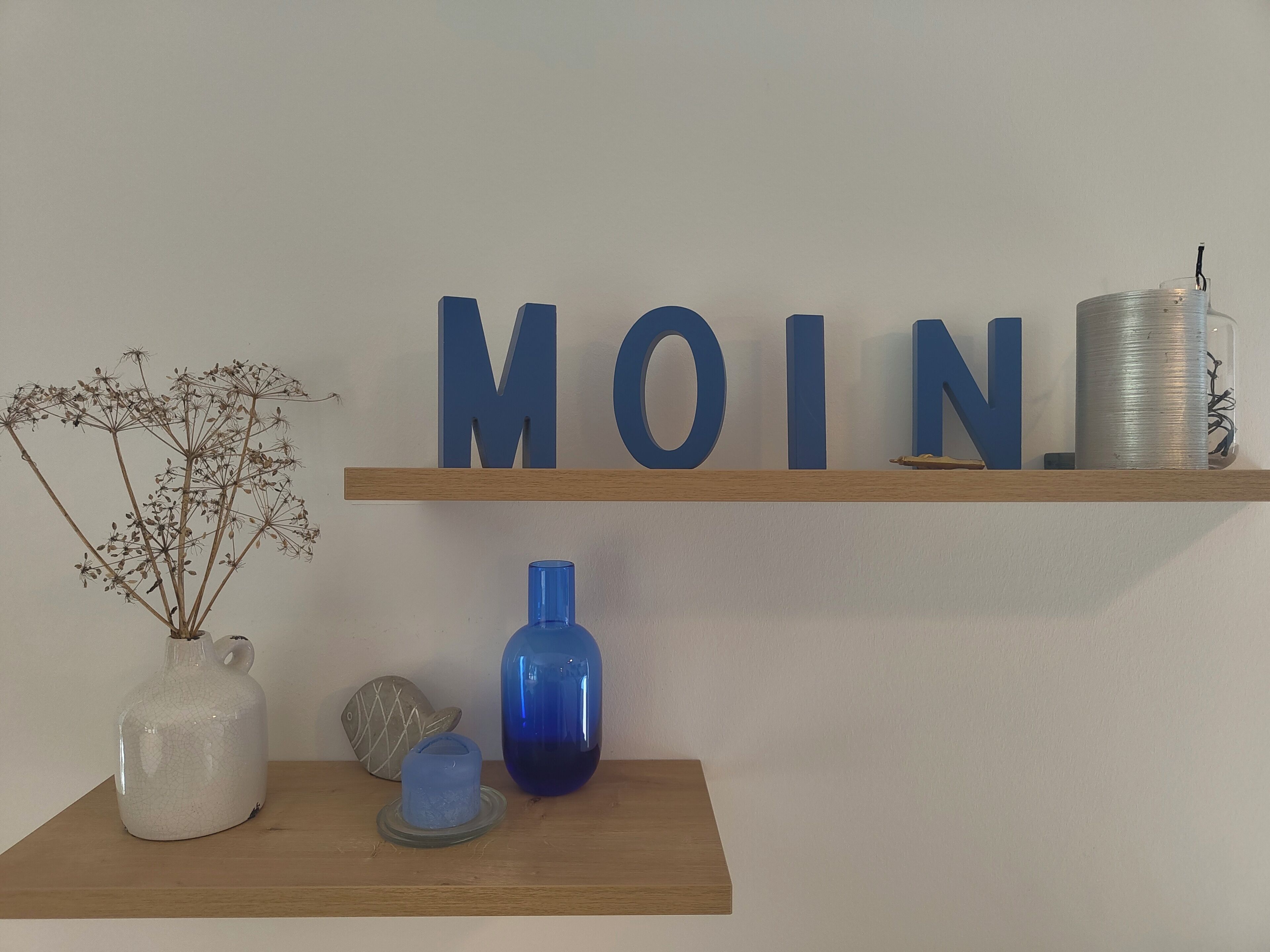 A wooden shelf with decorative items including a white ceramic jug, a blue vase, and a blue bottle.