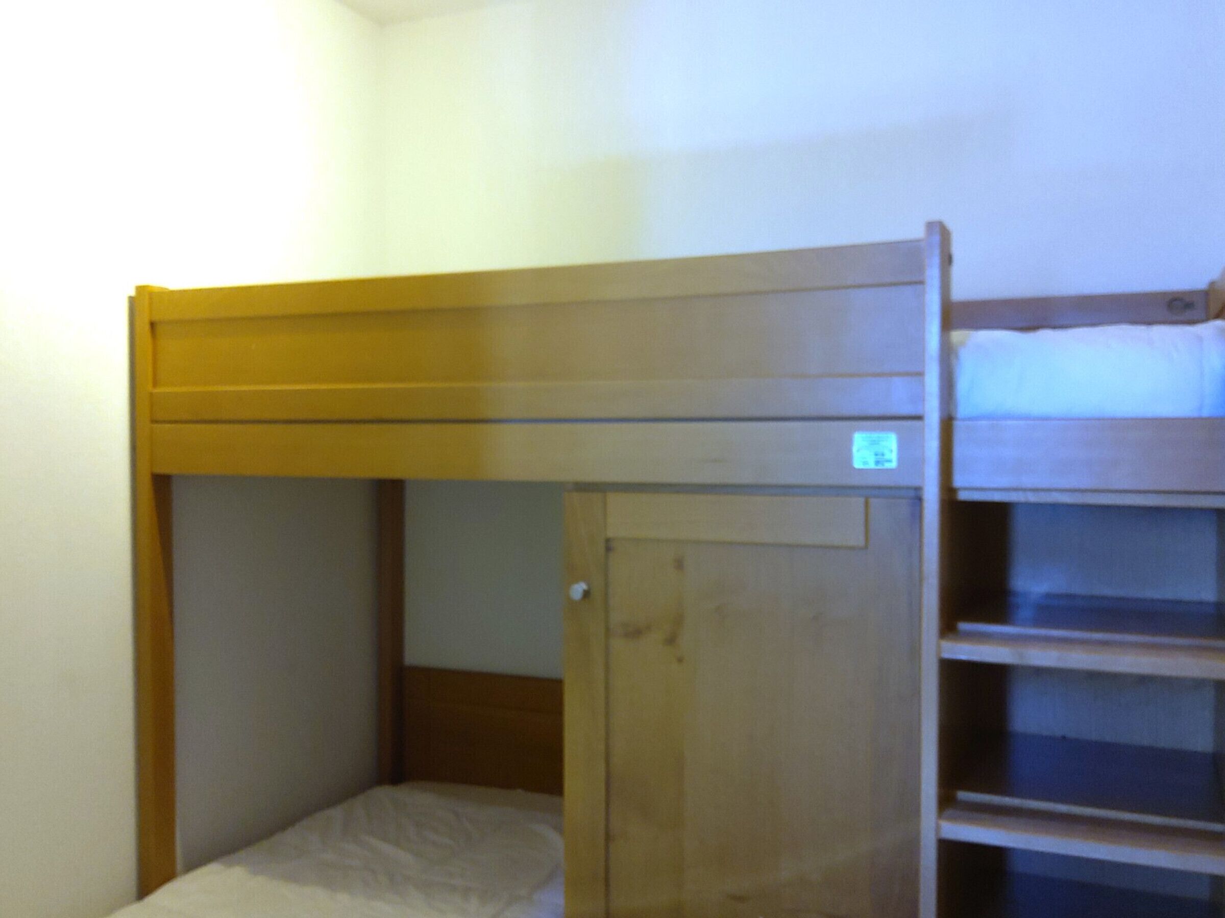 A bunk bed with a wooden frame and a single bed below.