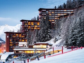 A modern ski resort with multi-story buildings, ski lifts, and snow-covered trees. - Arc 1600: 3-room apartment, sleeps 8, pool, parking (Les Arcs 1600)