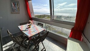 Ein Essbereich mit Tisch und Stühlen, einem Bild an der Wand und einem großen Fenster mit Blick auf Strand und Meer.