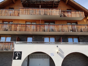 A multi-story building with wooden balconies, stone facade, and a sign indicating a ski resort.