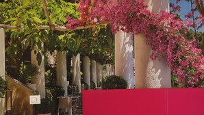 Un dormitorio con cabecera roja, cama blanca y lámpara rosa.