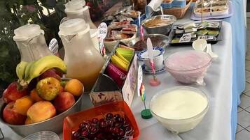 A buffet table with various food items, including fruits, beverages, and desserts.