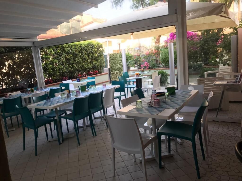Un área de comedor al aire libre con mesas y sillas, rodeada de follaje y una sección cubierta.