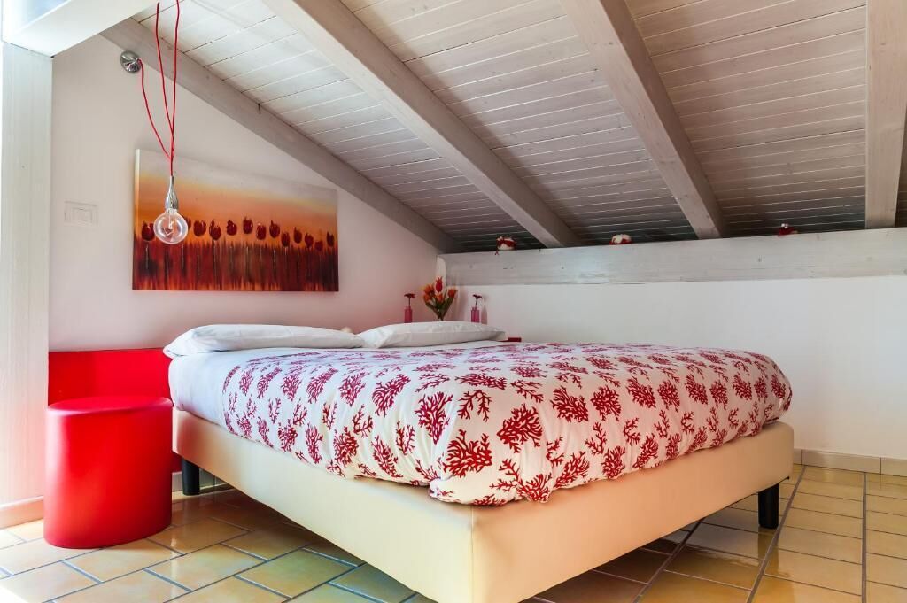 Ein Schlafzimmer mit einem Bett, einem roten Sessel, einem Gemälde und einem gefliesten Boden.