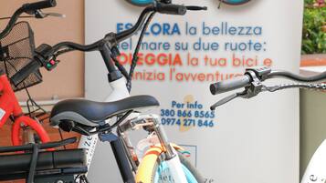 A bicycle parked in front of a sign with a bicycle illustration and contact information.