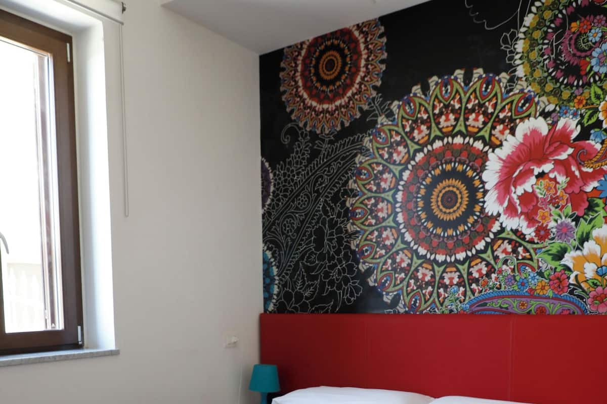A bed with a red headboard, a blue bedspread, and a colorful tapestry on the wall.