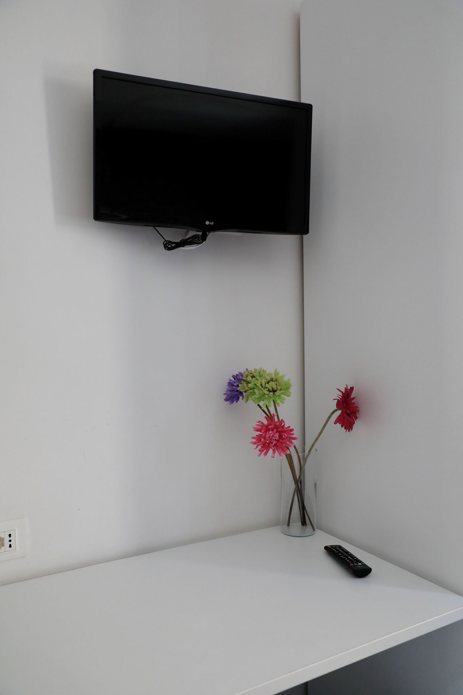 Et hvidt tv-skab med et fladskærms-tv monteret over det. Der er en vase med blomster og en fjernbetjening på skabet.