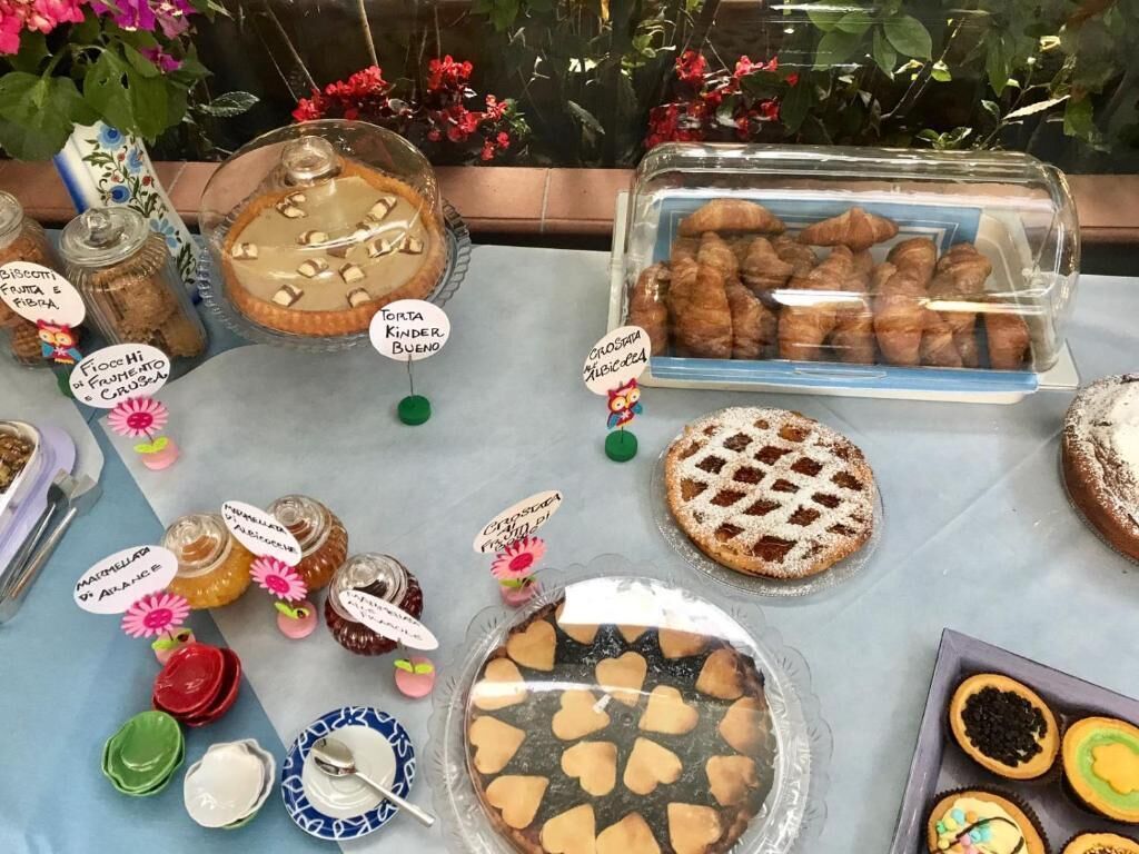 Verschiedene Desserts und Gebäckstücke sind auf einem Tisch ausgestellt, darunter ein Kuchen mit Gitterteig, eine Korb mit Croissants und mehrere Gläser Marmelade.