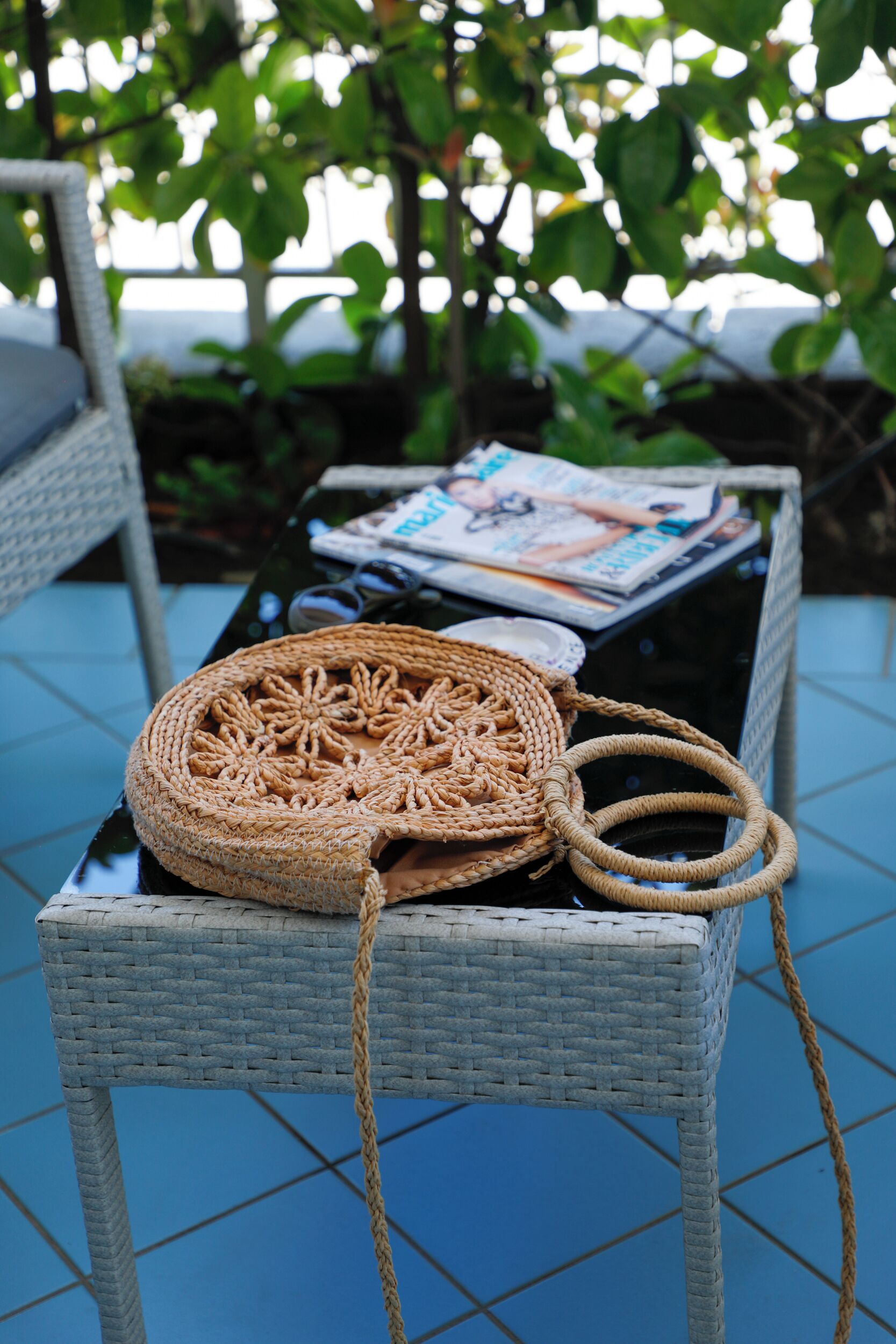 A wicker chair with a woven bag and magazines on a glass table.