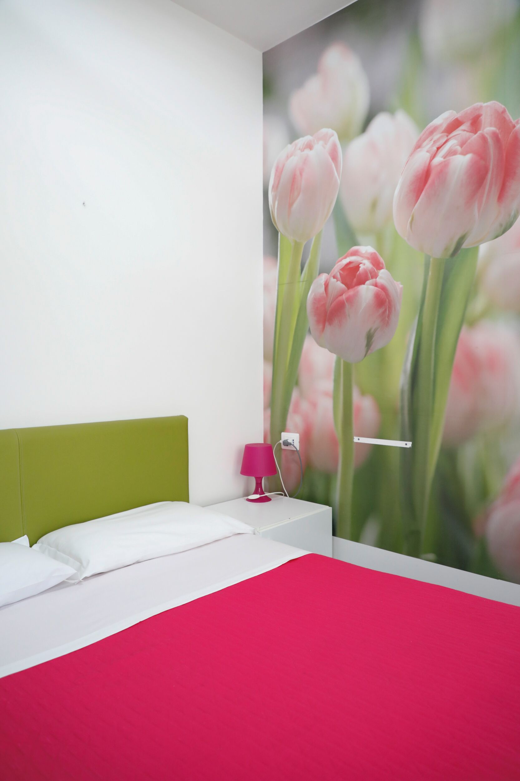 Ein Schlafzimmer mit einem grünen Kopfteil, weißer Bettwäsche und einer pinkfarbenen Lampe auf einem Nachttisch.