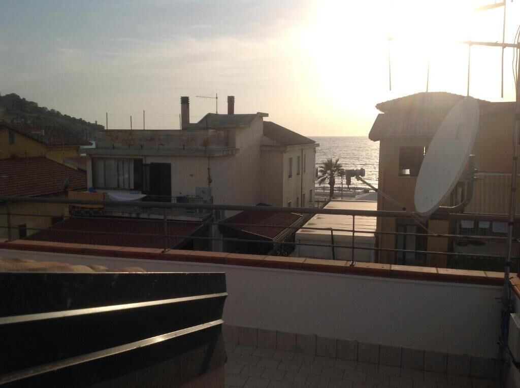 Eine Dachterrasse mit Blick auf das Meer, einer Satellitenschüssel und einem Gebäude mit roten Ziegeldach.