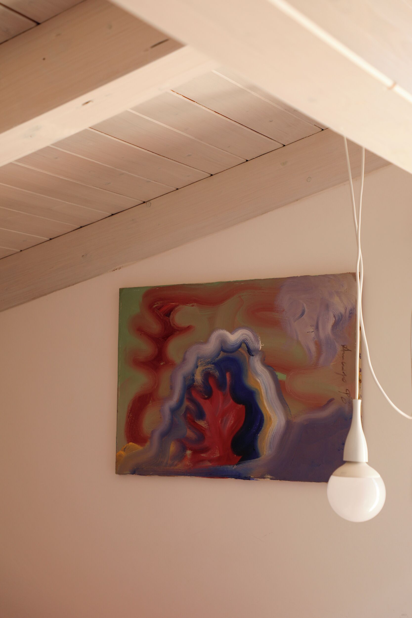 Una stanza con soffitto in legno, un quadro astratto dai colori vivaci al muro e una lampada a sospensione bianca.