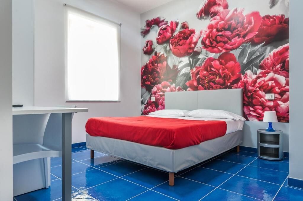 A bedroom with a bed, a desk, and a wall with a floral mural.