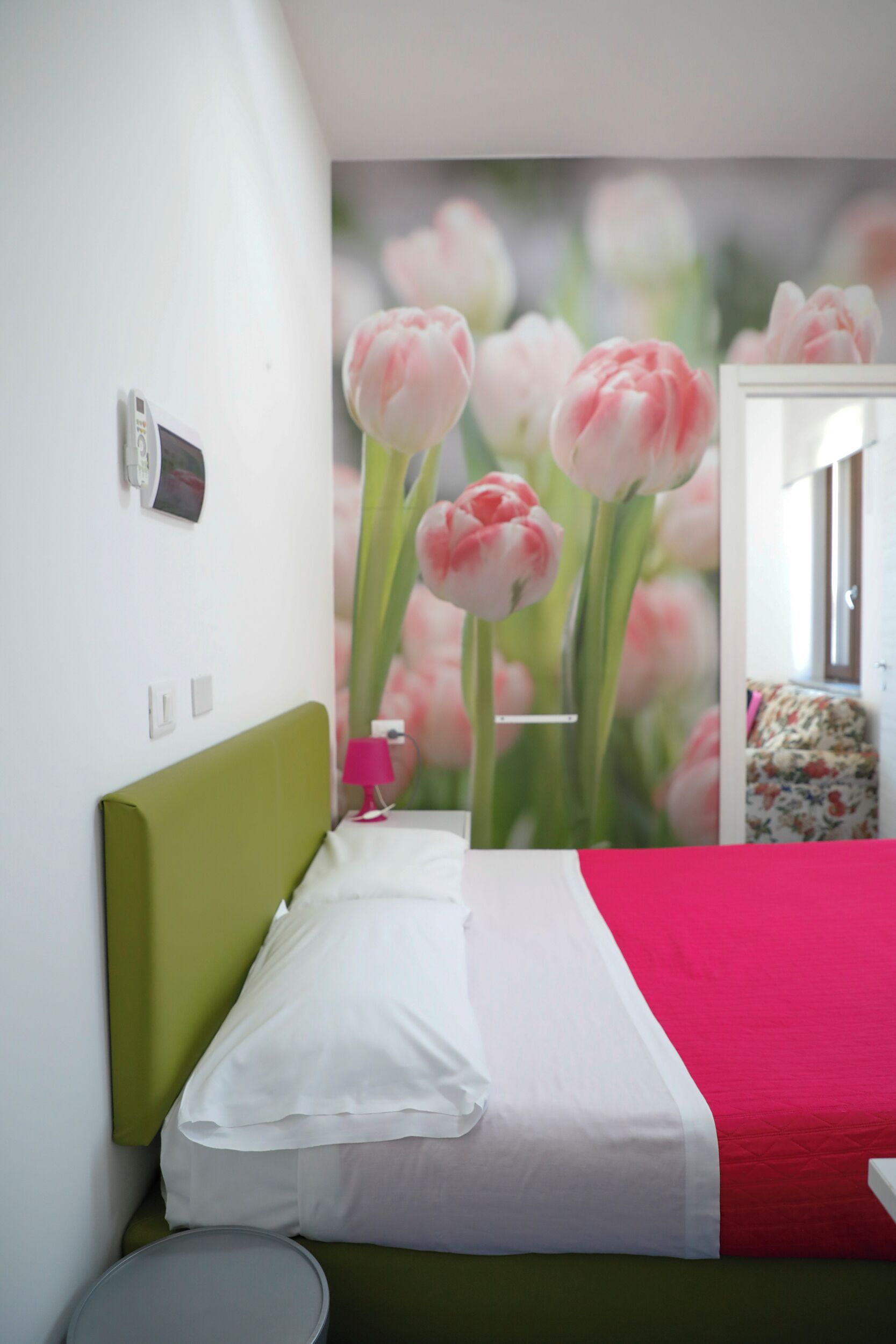 Een slaapkamer met een groen hoofdeinde, wit beddengoed en een rode accentkleur.