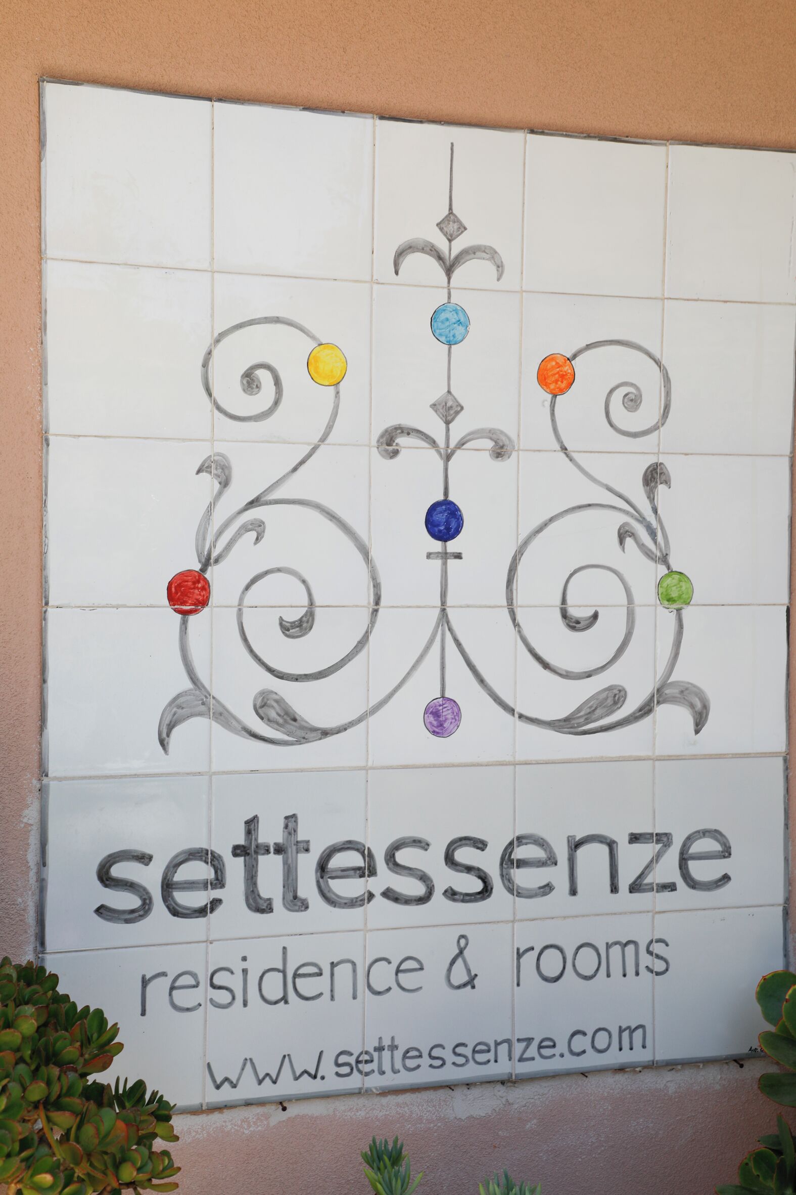 A sign for 'settessenze residence & rooms' with decorative swirls and colored dots.