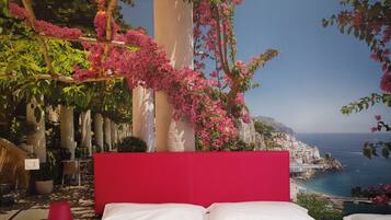 A bed with white linens, a red headboard, and pink flowers in the background.