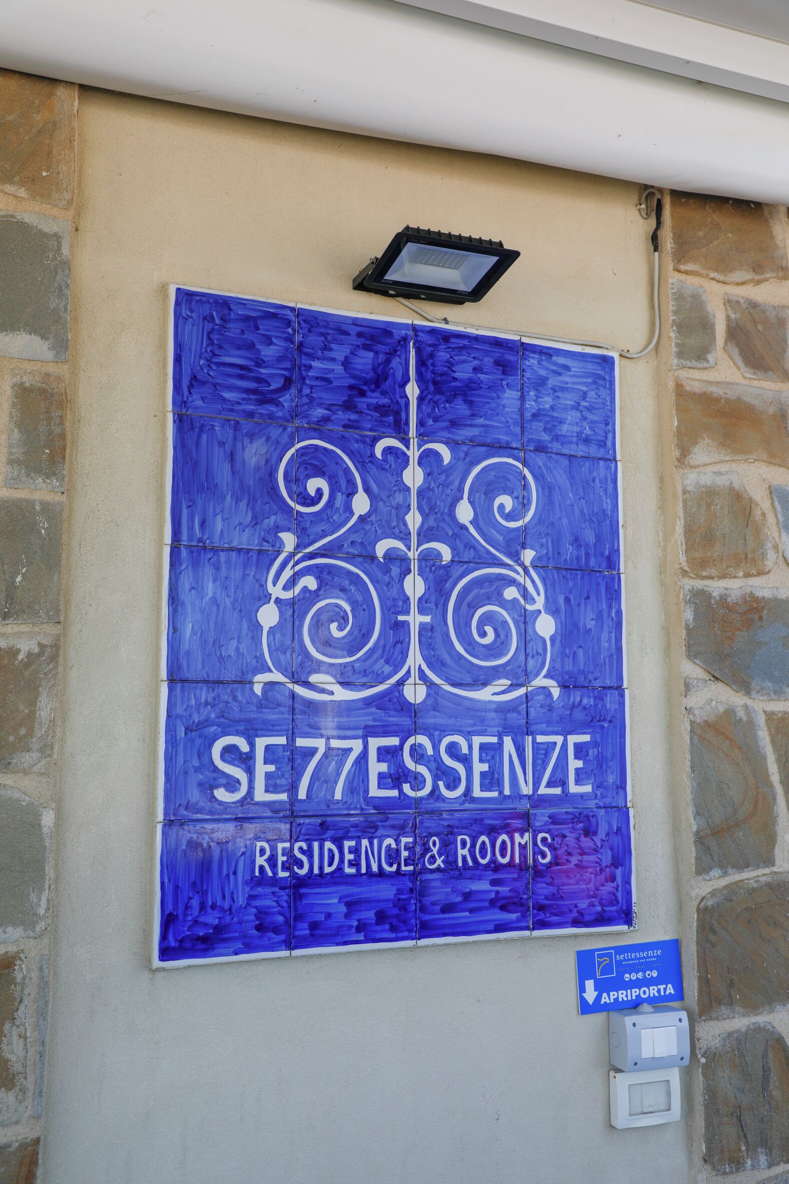 A blue sign with "SE77ESSENZE RESIDENCE & ROOMS" and an arrow pointing to "APRIPORTA".