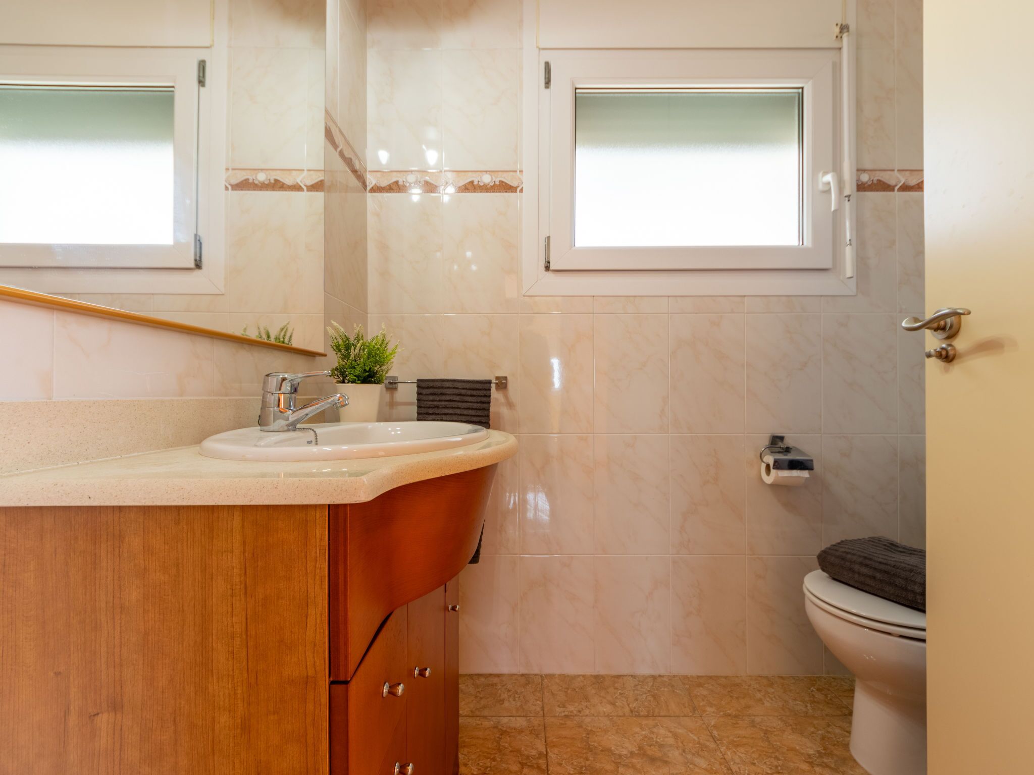 A bathroom with a sink, mirror, toilet, and a window.
