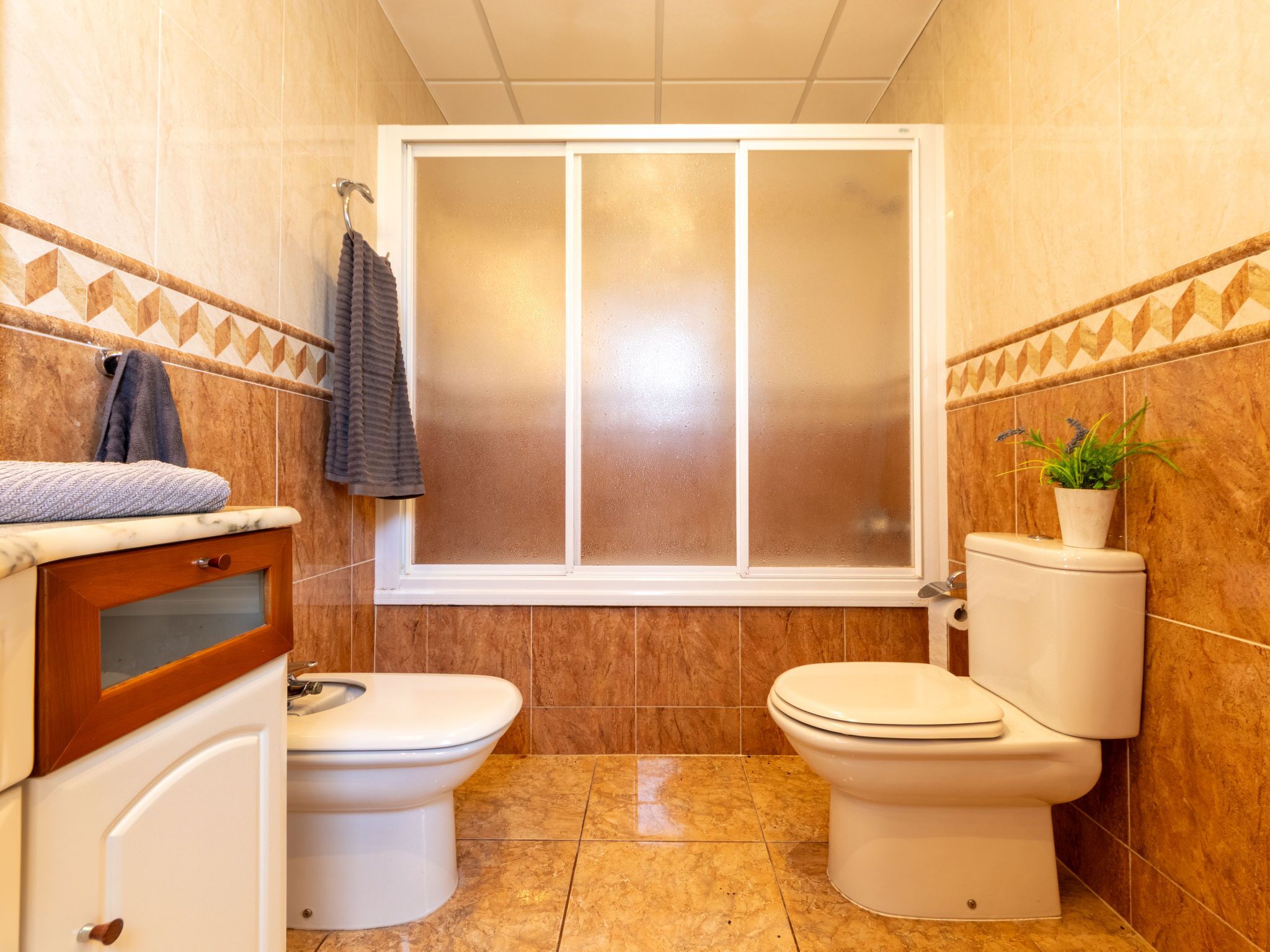 Une petite salle de bain comprenant deux toilettes, un espace douche et un meuble-lavabo avec un porte-serviettes.
