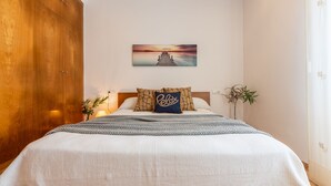 A bedroom with a large bed, a wooden wardrobe, a wall-mounted painting, and a potted plant. - Vacation home Dani by Interhome (L'Ampolla)