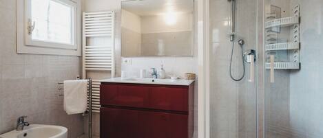 A modern bathroom with a bidet, a sink, a mirror, and a glass-enclosed shower.