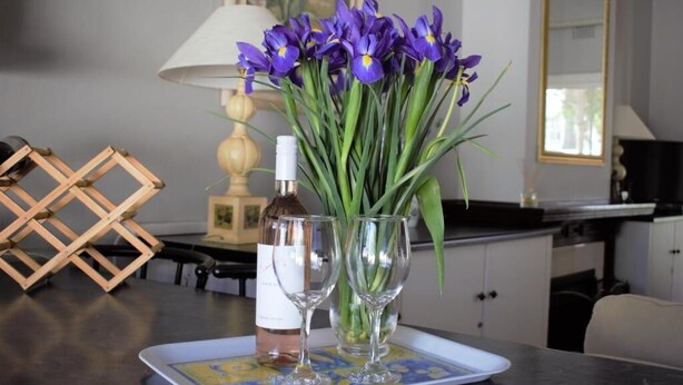 A table with a bottle of rose wine, two wine glasses, and a bouquet of purple flowers. - Quaint family home close to Tram terminal (Franschhoek)