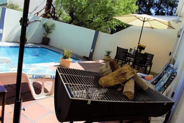 A backyard with a swimming pool, a grill, outdoor furniture, and potted plants.