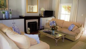 A living room with a beige sofa, a glass coffee table, and a fireplace. - Quaint family home close to Tram terminal (Franschhoek)