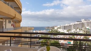Un balcón con vista a un paisaje urbano costero, que incluye un hotel y edificios residenciales.