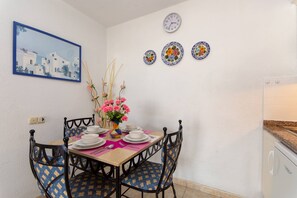 Un coin repas avec une table dressée pour quatre personnes, des chaises à l’habillage à motifs, un vase rempli de fleurs et des assiettes décoratives accrochées au mur.