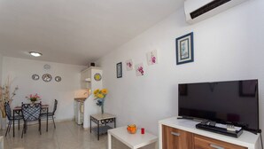 Una sala de estar moderna con un televisor de pantalla plana, un comedor con sillas y una mesa, y una cocina con armarios y un lavamanos.