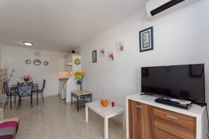 Een moderne woonkamer met een flatscreen televisie, een eethoek met stoelen en een tafel, en een keuken met kastjes en een spoelbak.