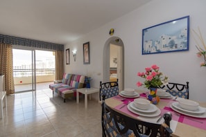 A dining area with a table set for four, a sofa, and a balcony with a view. - Santa Maria 85 - One Bed (Costa Adeje)