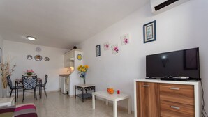 Sala de estar con televisor, comedor con sillas y una mesa, y área de cocina con refrigerador y pileta.