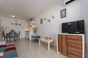Een woonkamer met een televisie, een eethoek met stoelen en een tafel, en een keuken met een koelkast en een spoelbak.
