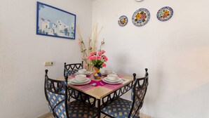 Un comedor con una mesa dispuesta para cuatro, sillas, un jarrón con flores, un reloj y un cuadro en la pared.