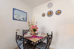 Een eetgedeelte met een tafel voor vier personen, stoelen, een vaas met bloemen, een klok en een ingelijste foto aan de muur.