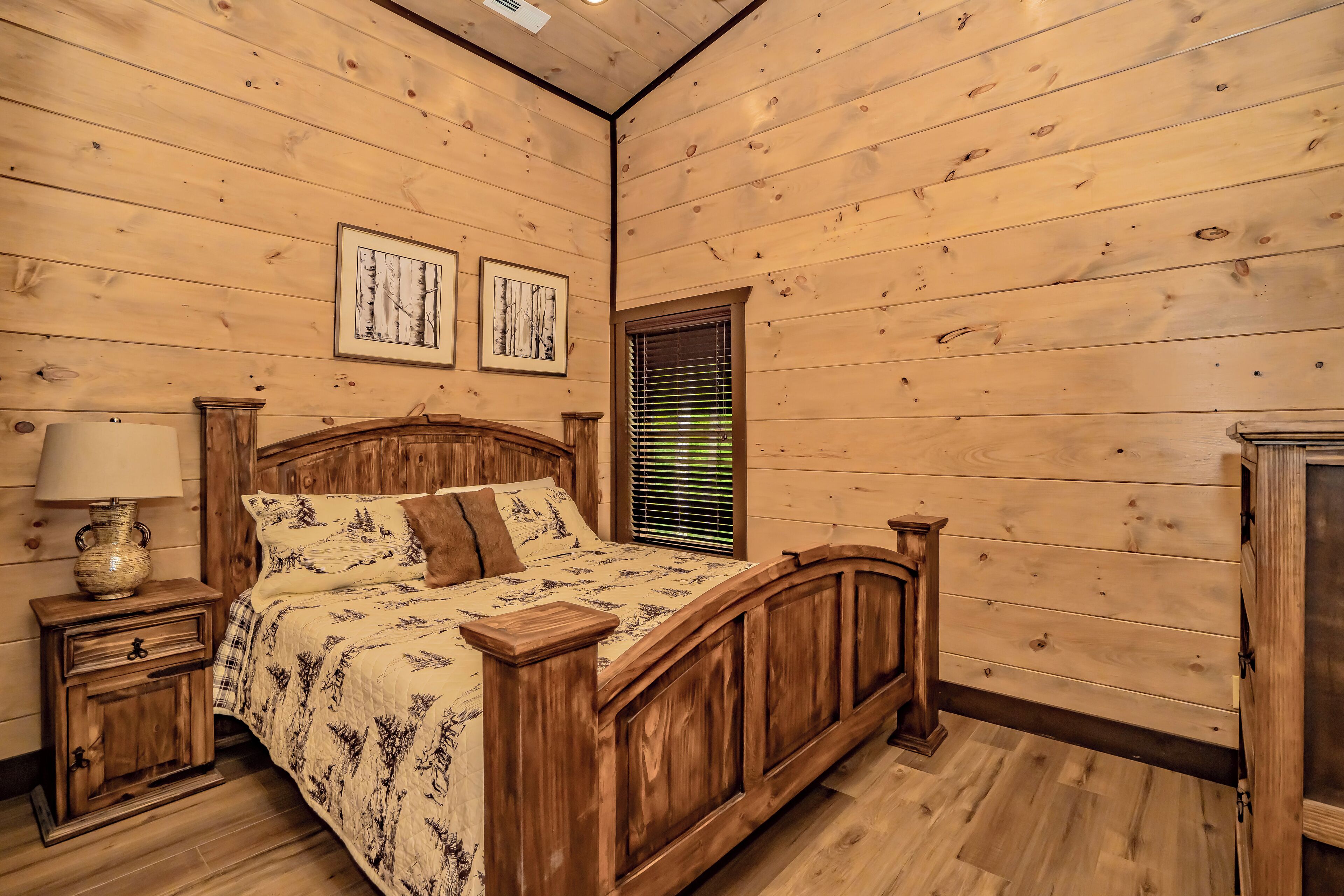 A wooden-paneled bedroom with a bed, nightstand, lamp, and framed pictures on the wall.