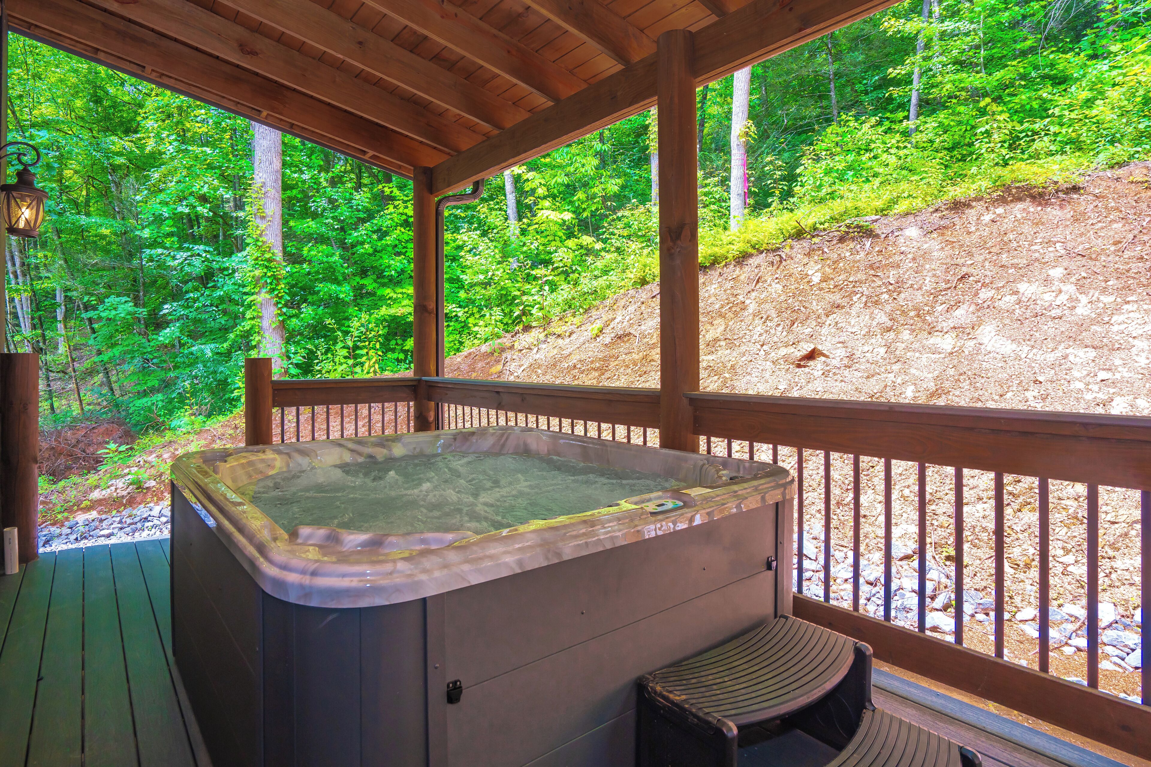 A wooden deck with a hot tub and a bench, overlooking a forested area.