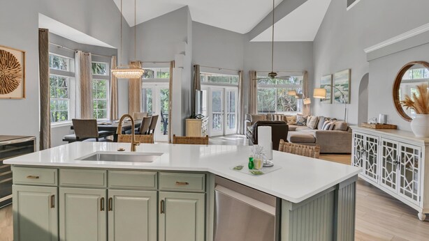 A spacious kitchen with a large island, a dining area with a chandelier, and a living room with a sofa and a TV. - Unique 3BR condo plus *LOFT* w/ golf cart & spacious open floor plan at Sandestin Golf & Beach Resort! (Miramar Beach)