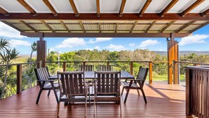A covered outdoor patio with a wooden table and chairs, surrounded by a metal railing, overlooking a scenic landscape. - Hibiscus Dreaming - Brooms Head Village Location (Brooms Head)