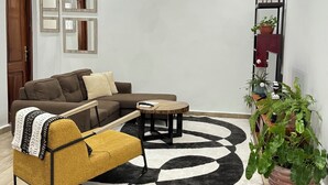 Un salon moderne avec un canapé d’angle, une table basse et un fauteuil jaune. Un miroir décoratif est accroché au mur et une plante en pot se trouve dans un coin.