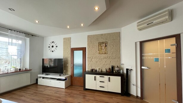 Una sala de estar moderna con un televisor de pantalla plana, piso de madera, un mueble blanco y una puerta con paneles de vidrio esmerilado.