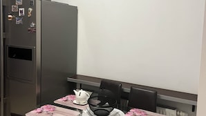 Un comedor con una mesa de vidrio, sillas, un hervidor de té, una cubierta de malla negra y un cuadro en la pared.