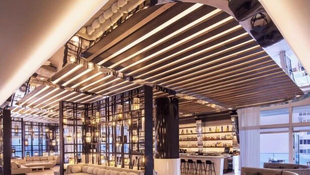 A modern interior with a bar area, seating, and a high ceiling with linear lighting.