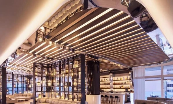 A modern interior with a bar area, seating, and a high ceiling with linear lighting.