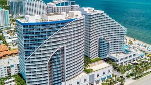 A high-rise hotel with multiple balconies, a swimming pool, and a view of the ocean.
