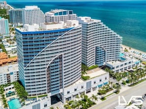 A high-rise hotel with multiple balconies, a swimming pool, and a view of the ocean.